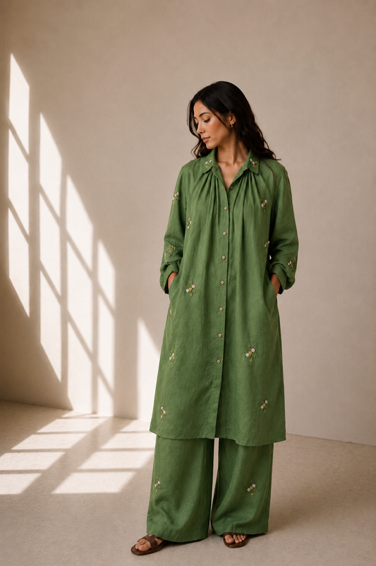 Woman wearing a linen green outfit with roses embroidery in a softly lit room.